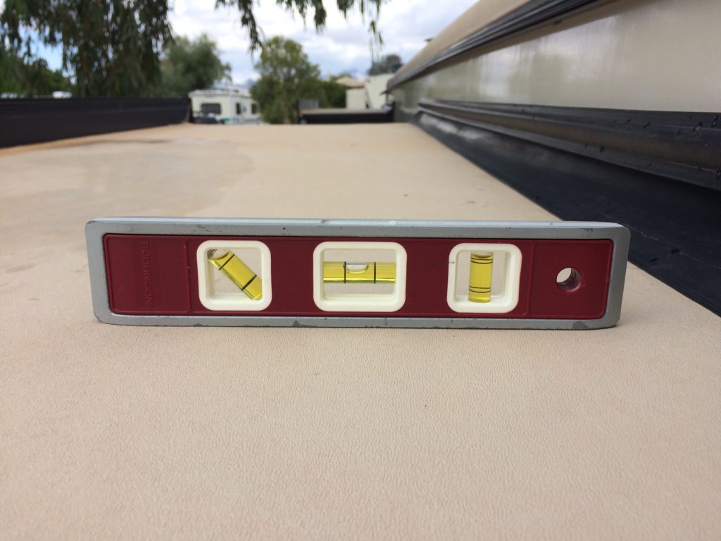 A level checking tool on the roof of an RV slide. The level bubble indicates the slide is angled down and towards the body of the RV.