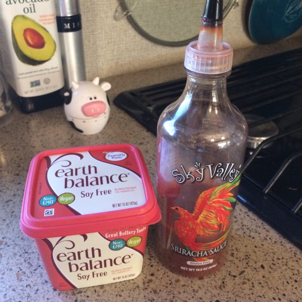 A bottle of sriracha next to a container of Earth Balance