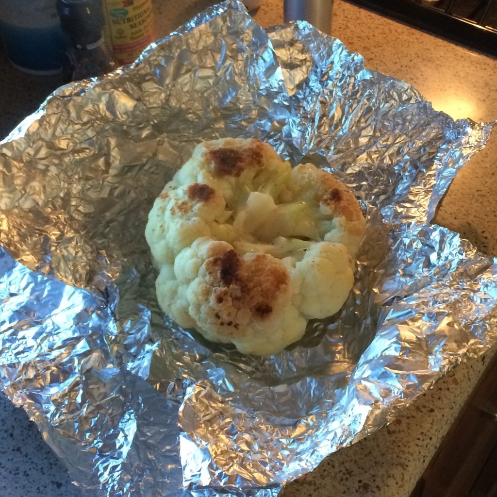 A head of cauliflower with charred edges from the grill, sitting in an open foil wrapper.