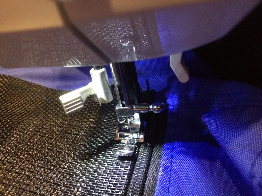 A closeup of a sewing machine needle sewing the new screen in place.