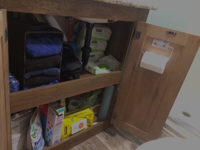 An open bathroom cabinet with two shelves filled with towels and other bathroom items, and a toilet paper holder on the inside of the cabinet door.