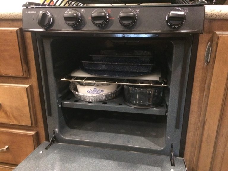 An oven with neatly stacked backware on two shelves.