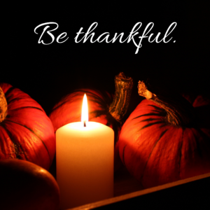Pumpkins lit by a candle with the text "Be thankful."