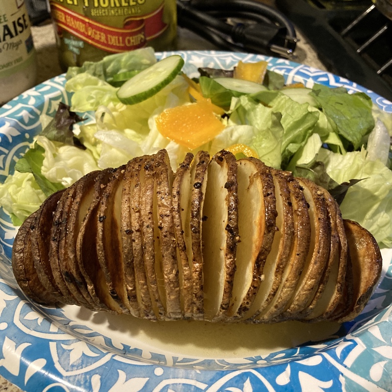 A browned potato with slices fanned out and a salad  