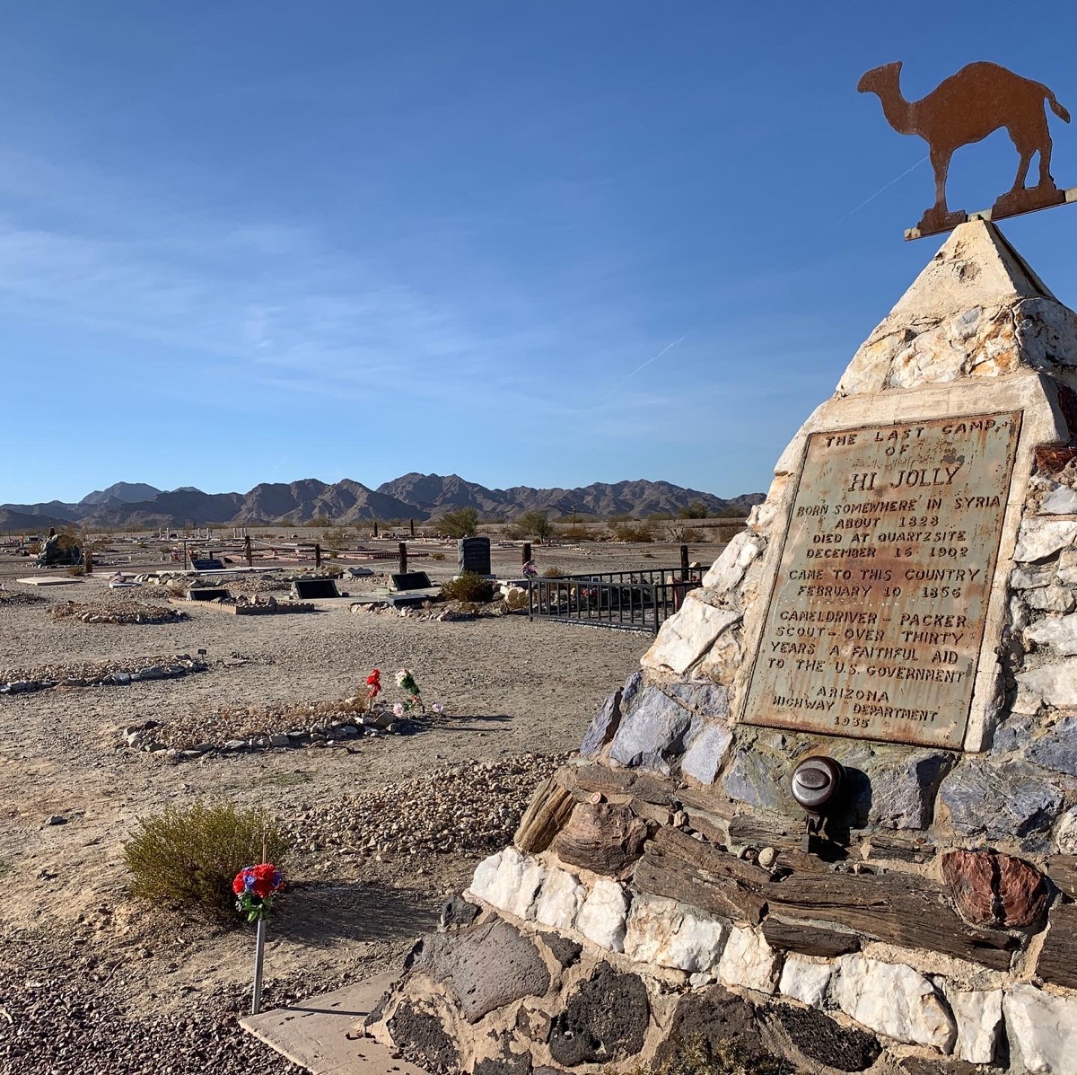 A stone pyramid monument with blue skies and a cemetery in the background  