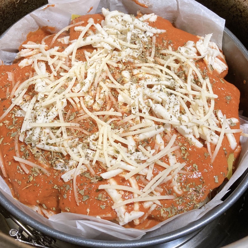 unbaked lasagna in a pan with parchment covered in raw cheese