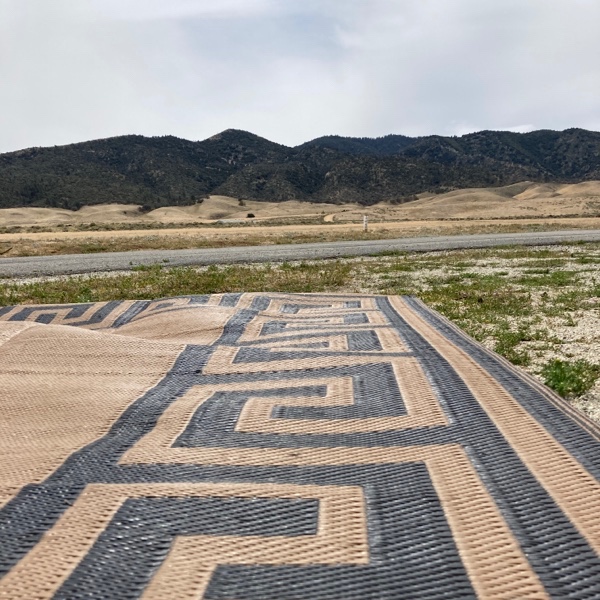 Looking out across a geometric print outdoor mat across a field and runway with many trees and gentle rolling hills in the background.