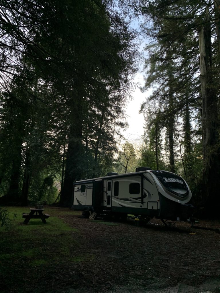 A camper next to many trees. It is very shady. 