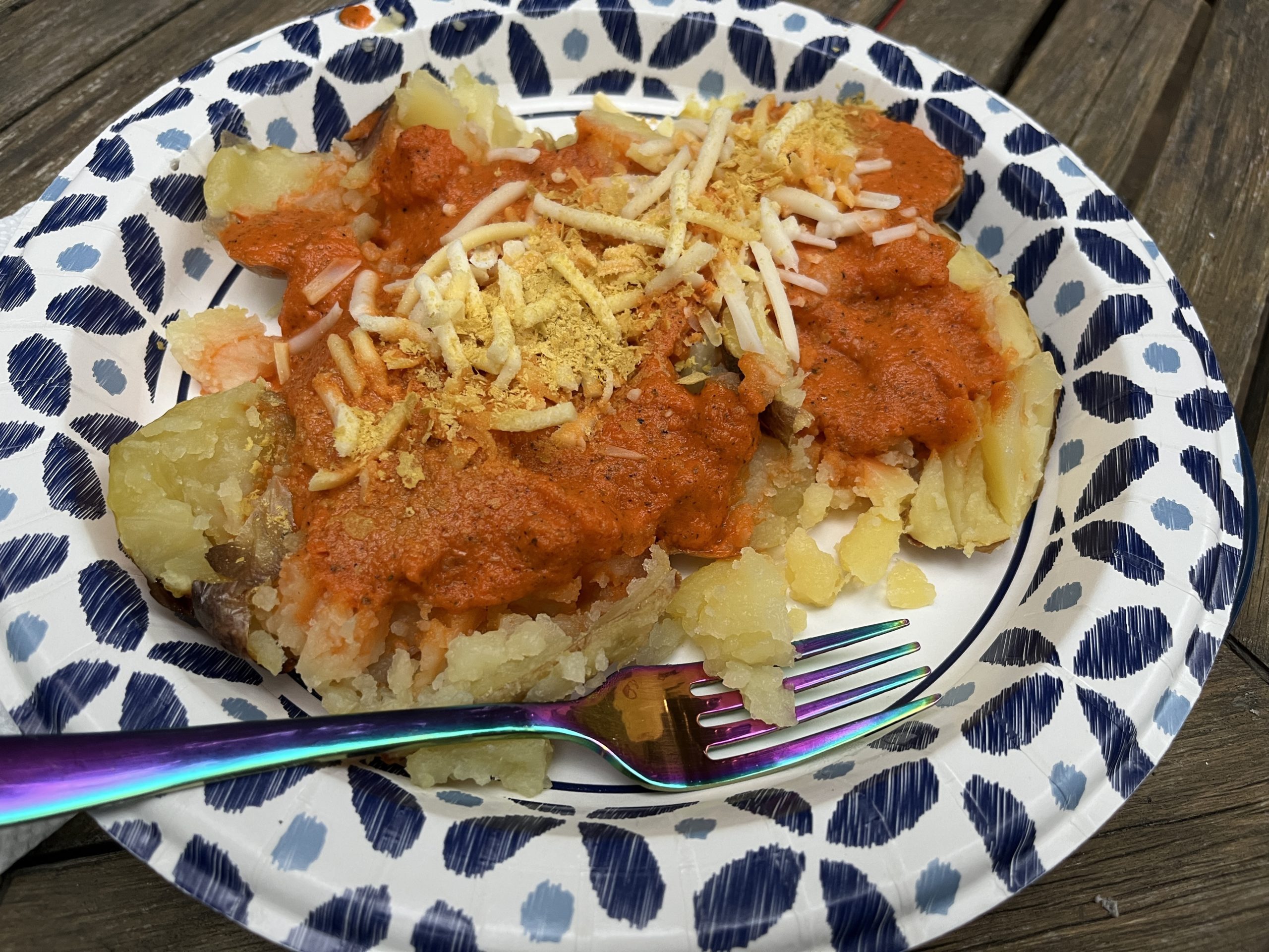 An open faced baked potato with orange sauce and shredded cheese. 